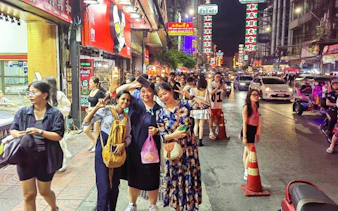 Night market street scene in Bangkok with people and tuk tuks.