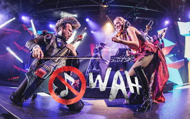 Musicians performing energetically on stage with WAH logo in foreground.