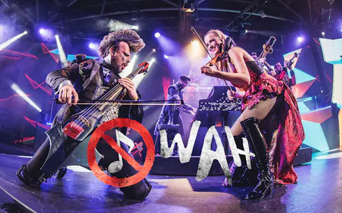 Musicians performing energetically on stage with WAH logo in foreground.