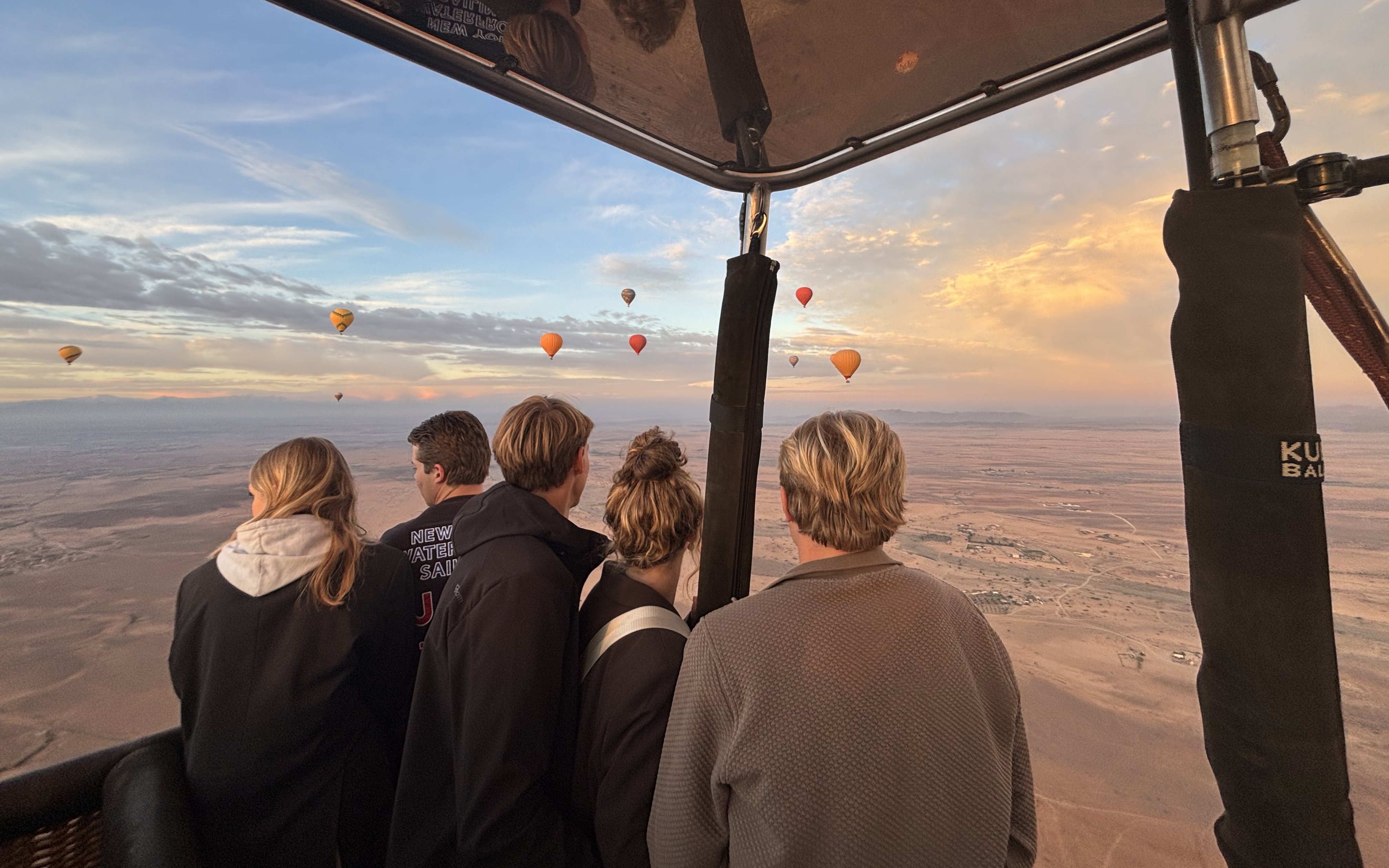 People enjoying view from hot air balloon over Marrakech desert.