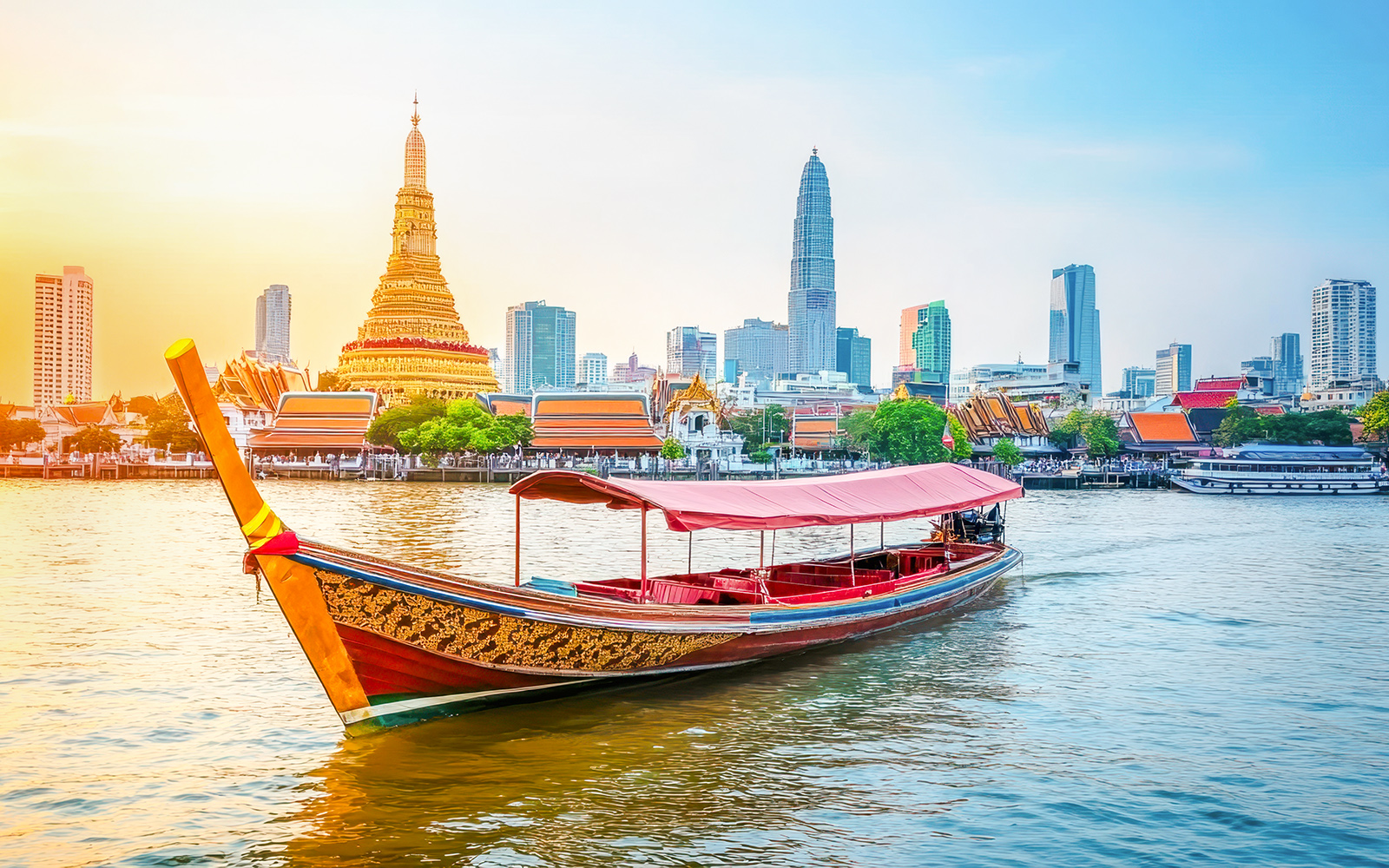 Traditional long-tail boat on Chao Phraya River with Bangkok skyline and Wat Arun in background.
