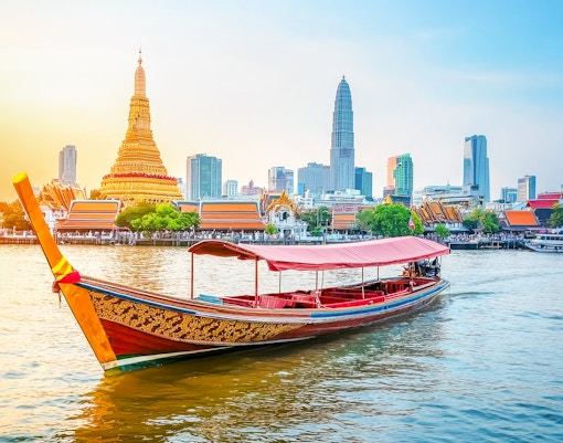 Traditional long-tail boat on Chao Phraya River with Bangkok skyline and Wat Arun in background.