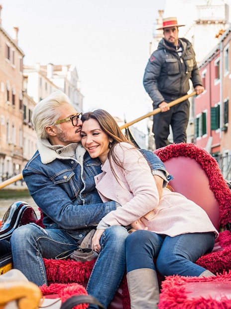 Couple enjoying a gondola ride in Venice canal with gondolier in the background.