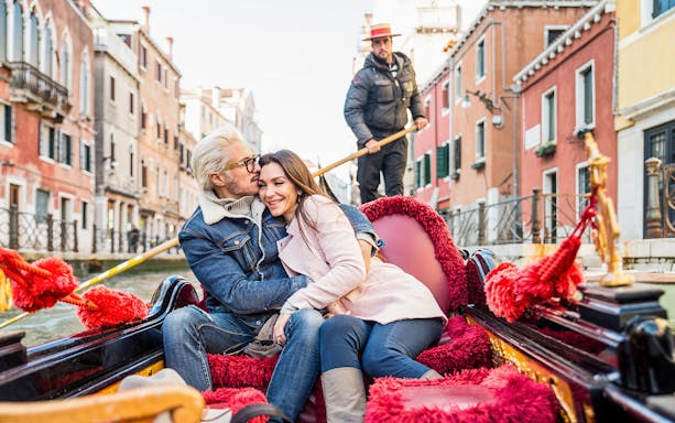 Couple enjoying a gondola ride in Venice canal with gondolier in the background.