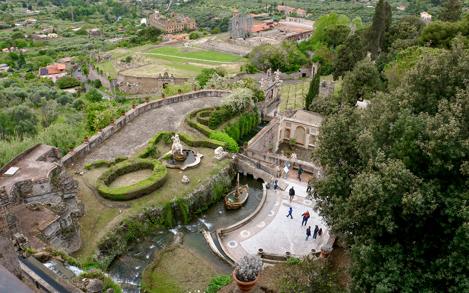 Tourists walking through the gardens of Villa d'Este in Tivoli, Italy, with fountains and sculptures.