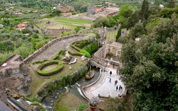 Tourists walking through the gardens of Villa d'Este in Tivoli, Italy, with fountains and sculptures.