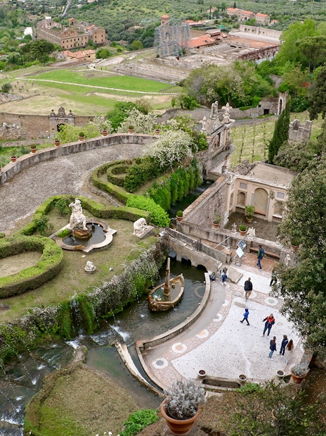 Tourists walking through the gardens of Villa d'Este in Tivoli, Italy, with fountains and sculptures.