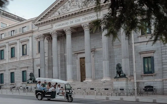 Tourists on an electric tuk-tuk in front of Congreso de los Diputados, Madrid, Spain.