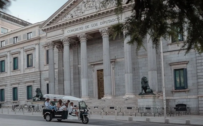 Tourists on an electric tuk-tuk in front of Congreso de los Diputados, Madrid, Spain.