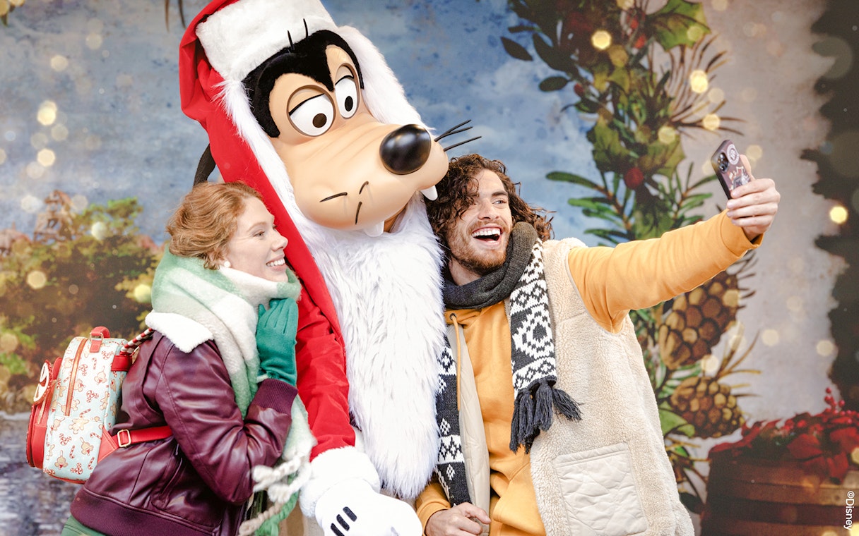 Tourists taking a selfie with Goofy during Disneyland Christmas 2025 celebrations.