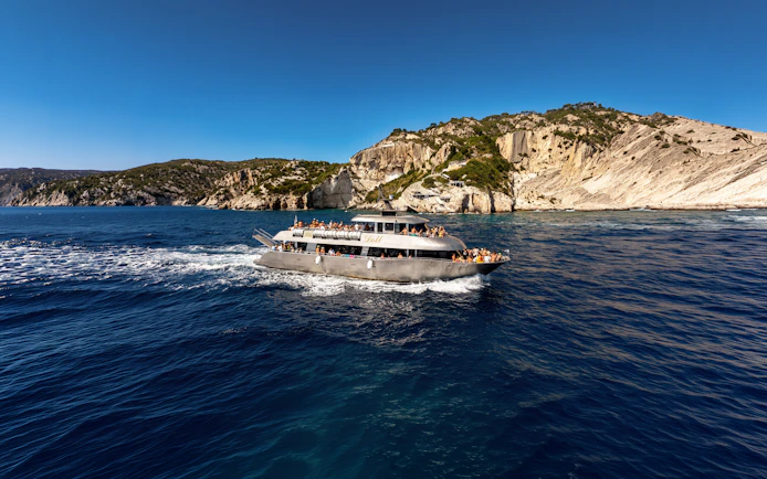 Cruise ship sailing near rocky coastline of Symi Island, Greece.