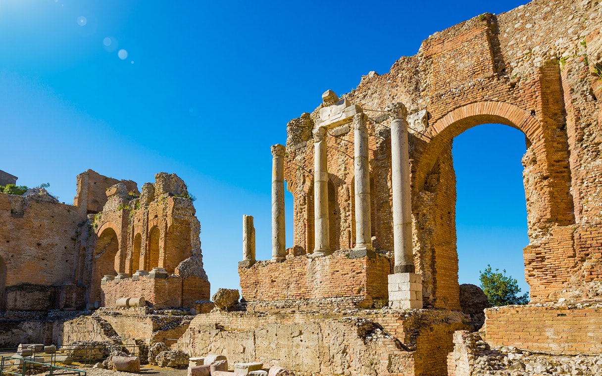 Taormina Ancient Theatre ruins with stone arches and columns under a clear blue sky.