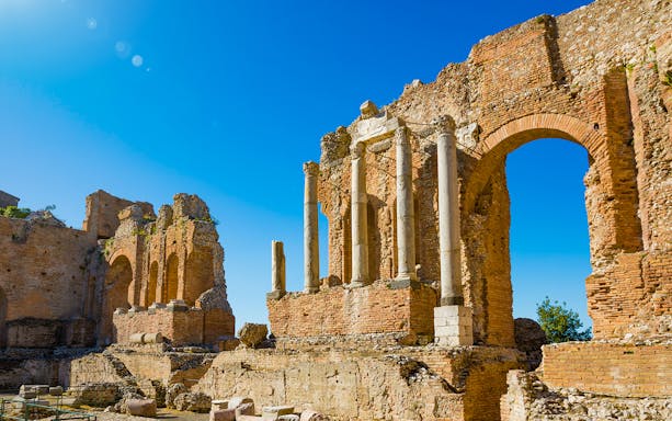 Taormina Ancient Theatre ruins with stone arches and columns under a clear blue sky.
