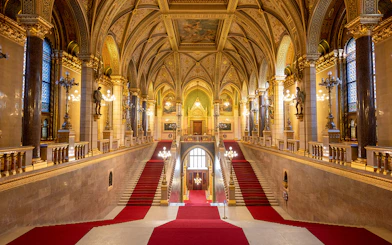 Grand Stairway inside Hungarian Parliament with ornate arches and red carpet.