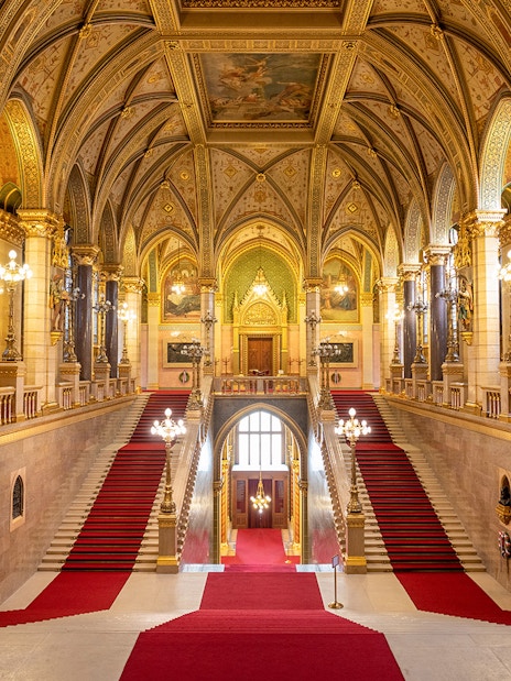 Grand Stairway inside Hungarian Parliament with ornate arches and red carpet.