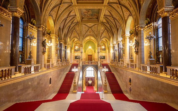 Grand Stairway inside Hungarian Parliament with ornate arches and red carpet.
