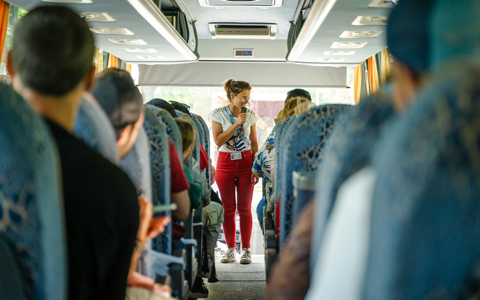 Tour guide speaking to passengers on a bus during a guided tour transfer.