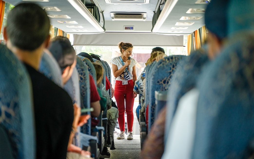 Tour guide speaking to passengers on a bus during a guided tour transfer.