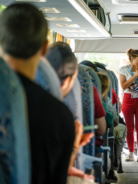 Tour guide speaking to passengers on a bus during a guided tour transfer.