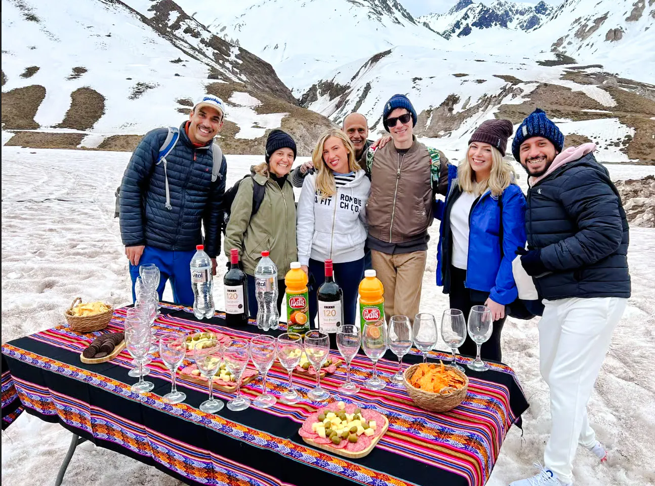 Group enjoying a picnic with drinks and snacks in snowy Cajon del Maipo, near Termas Baños Colina, Santiago.