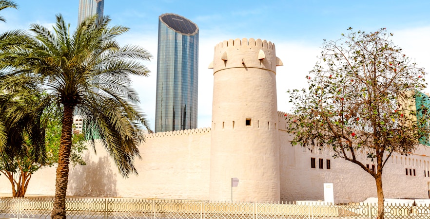 Qasr Al Hosn fort with modern skyscrapers in Abu Dhabi background.
