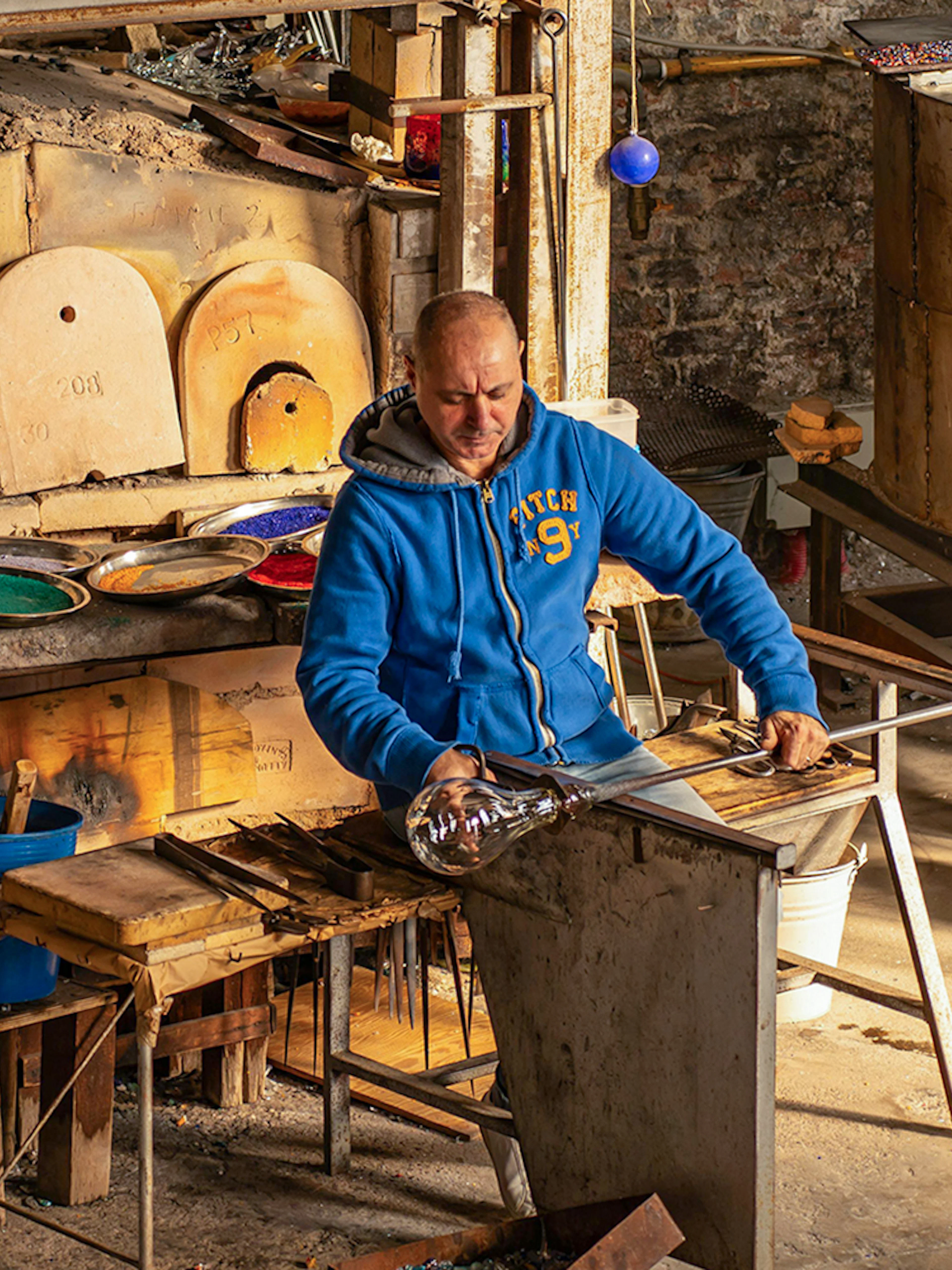 Artisan crafting glass at Murano workshop using traditional glass blowing techniques.