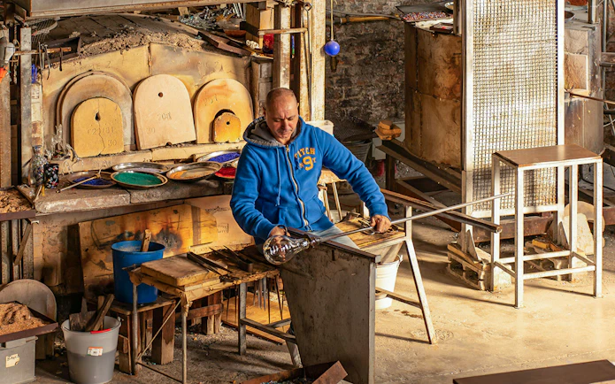 Artisan crafting glass at Murano workshop using traditional glass blowing techniques.