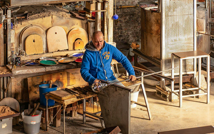 Artisan crafting glass at Murano workshop using traditional glass blowing techniques.