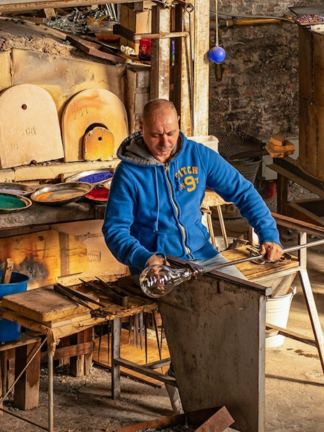 Artisan crafting glass at Murano workshop using traditional glass blowing techniques.