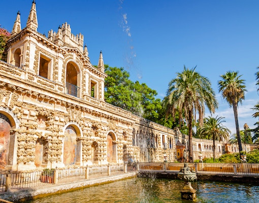 Alcazar palace's Mercury's pool with ornate architecture and palm trees in Seville, Spain.