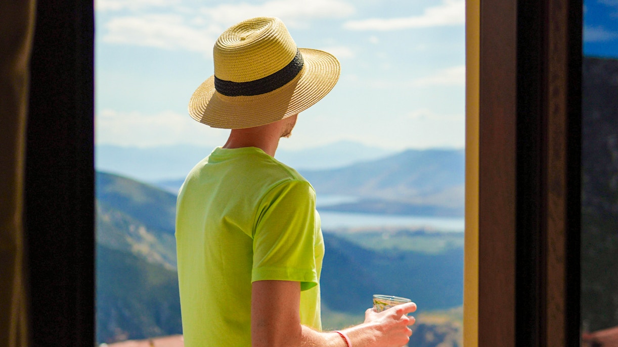 Man on hotel balcony overlooking Delphi, Greece, with mountains in the background.