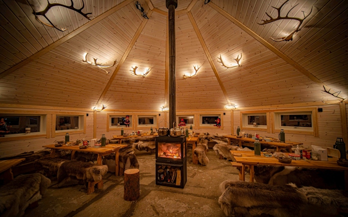 Wooden hut interior with central fireplace and reindeer hides, Tromso.