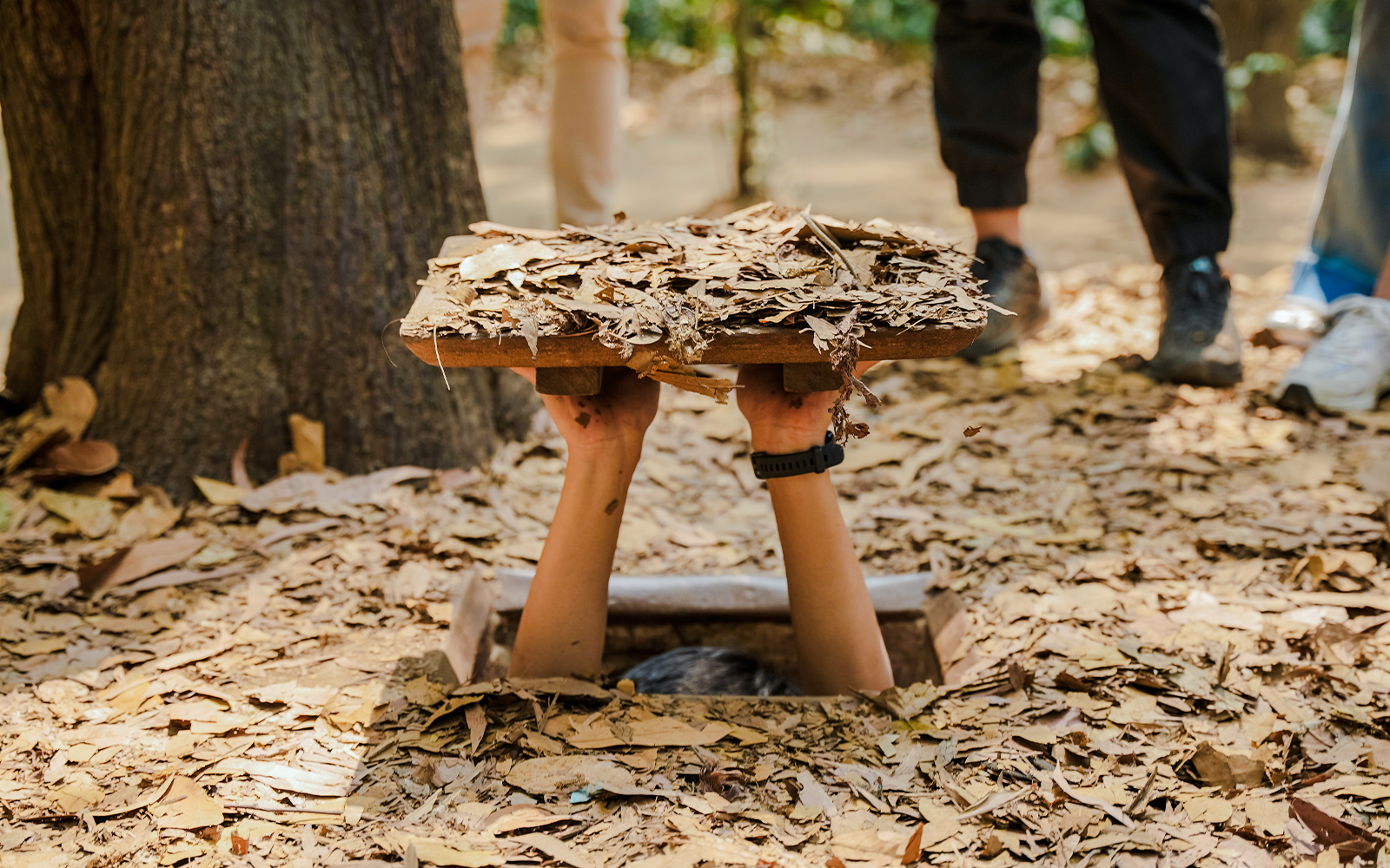 Hands lifting a camouflaged trapdoor in Cu Chi tunnels, Vietnam.