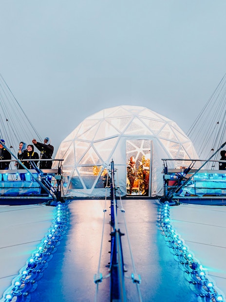 Visitors at the O2 Arena's snow globe experience, London, with illuminated walkway.