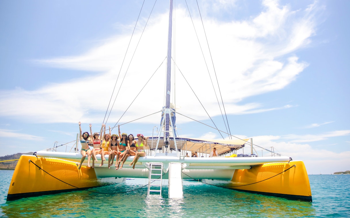 Women sitting on catamaran edge during South Sea Sailing tour, Fiji.