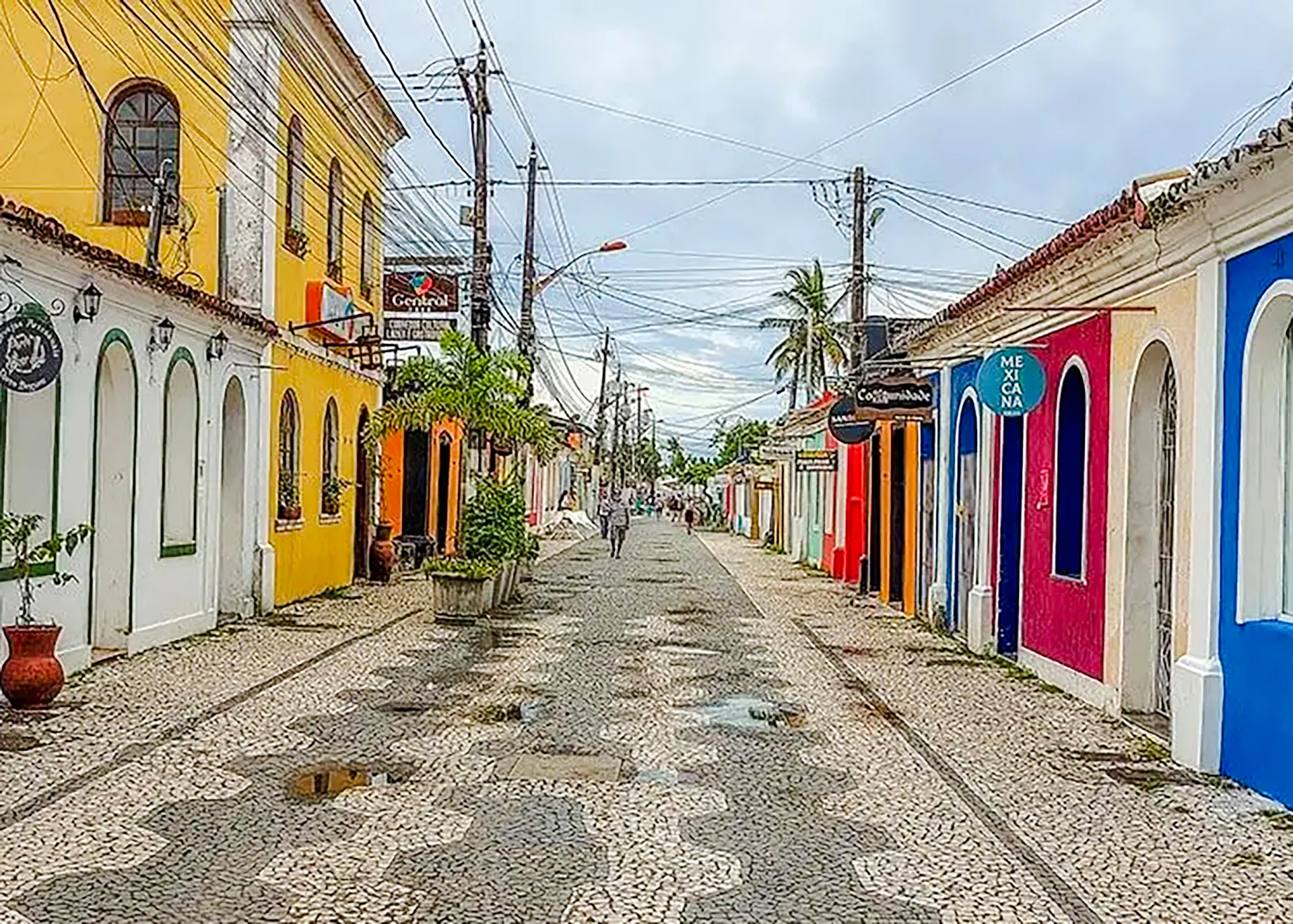 Colorful street in Arraial d'Ajuda, Porto Seguro, with cobblestone path and vibrant buildings.