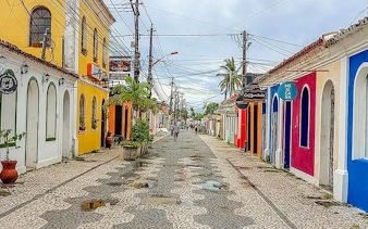 Colorful street in Arraial d'Ajuda, Porto Seguro, with cobblestone path and vibrant buildings.
