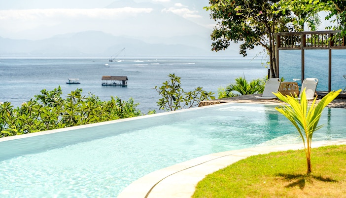 Infinity pool overlooking ocean view in Nusa Penida, with lounge chairs and tropical greenery.