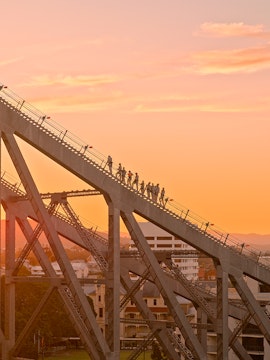 People climbing the Story Bridge in Brisbane at sunset.
