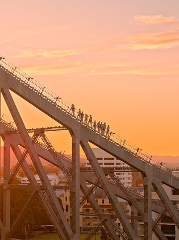 People climbing the Story Bridge in Brisbane at sunset.