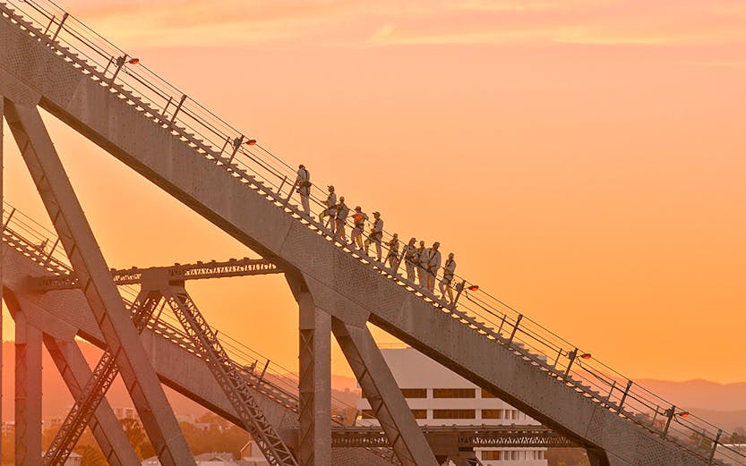 People climbing the Story Bridge in Brisbane at sunset.