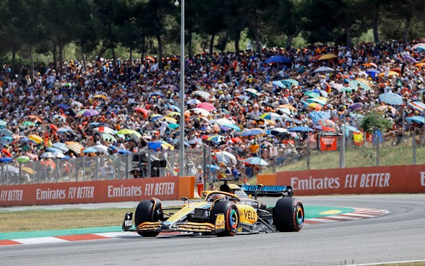 Formula 1 car racing on Barcelona track with crowd in background.
