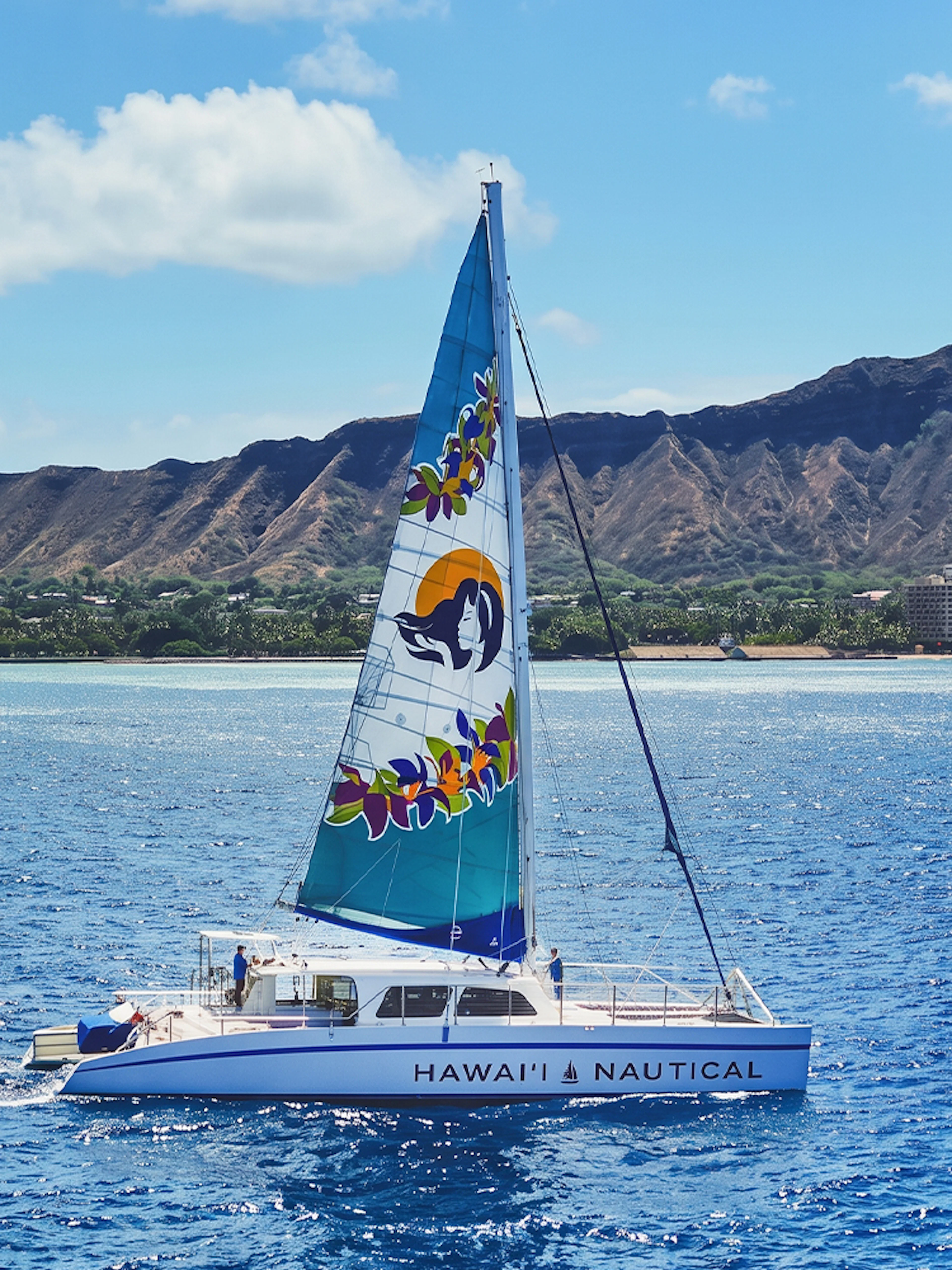 Catamaran sailing near Diamond Head, Waikiki, with scenic coastline in the background.