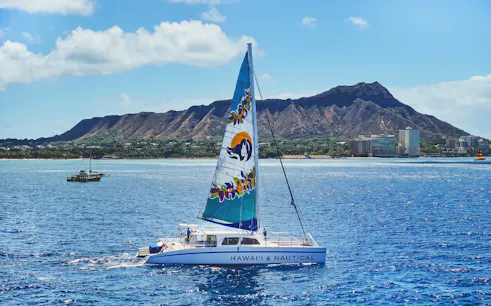 Catamaran sailing near Diamond Head, Waikiki, with scenic coastline in the background.