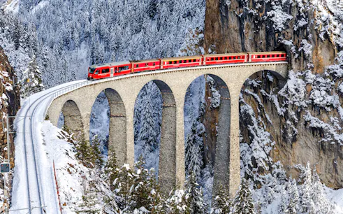 Red train crossing the Landwasser Viaduct in snowy Swiss Alps near St. Moritz.