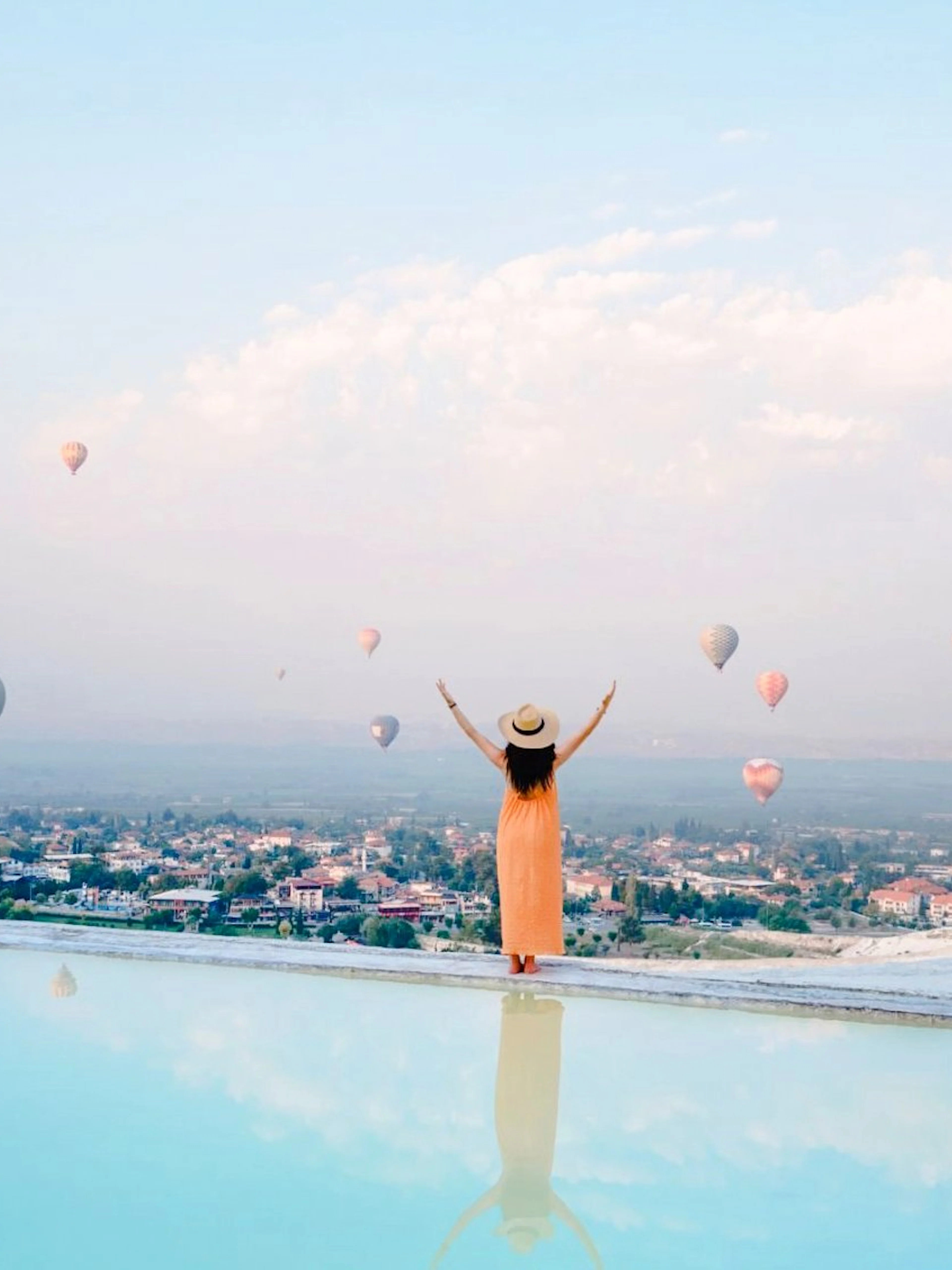 Hot air balloons floating above Pamukkale with a person enjoying the view.