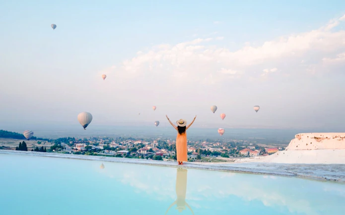 Hot air balloons floating above Pamukkale with a person enjoying the view.