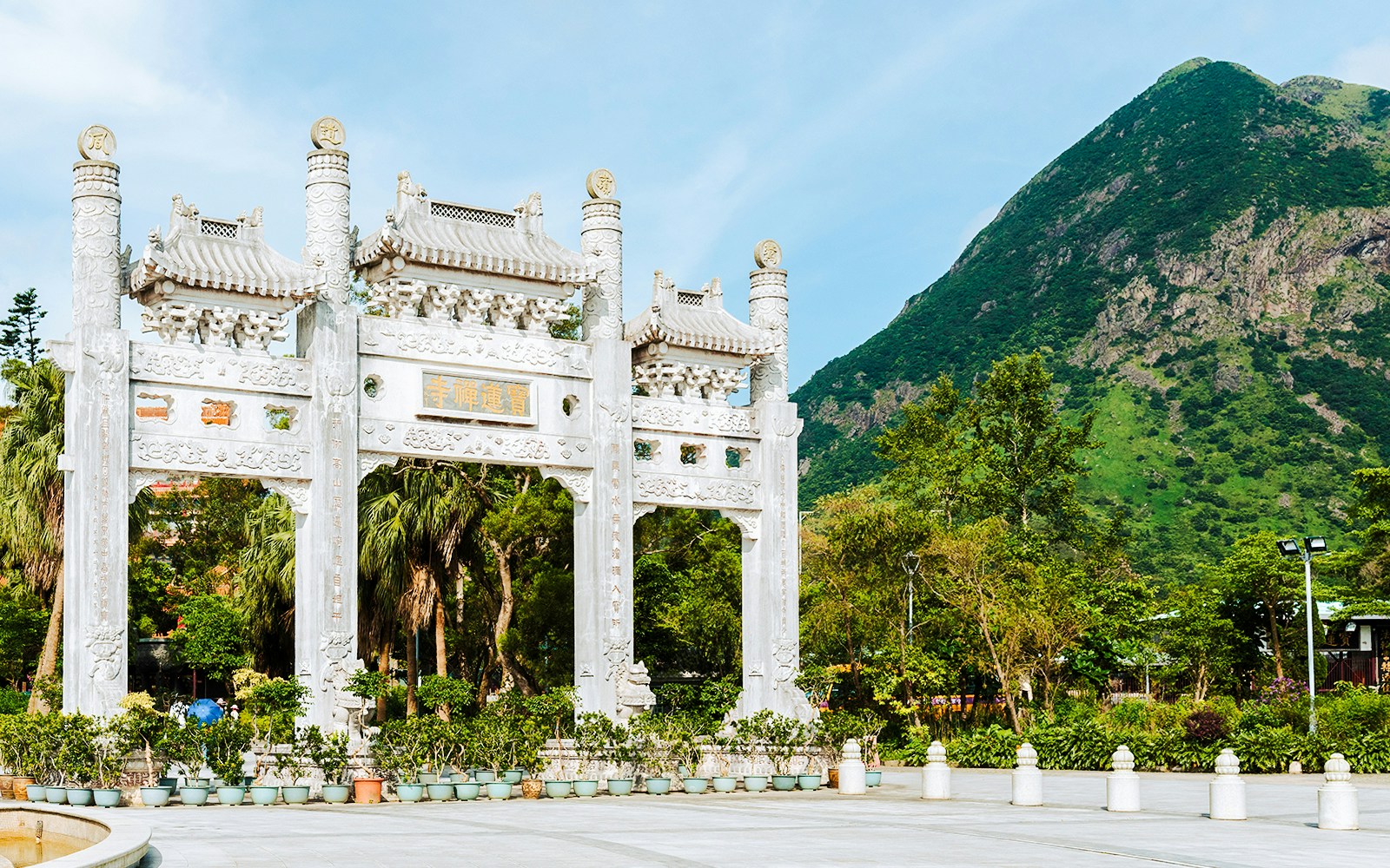 Ngong Ping Piazza arch with lush greenery and mountain backdrop in Hong Kong.