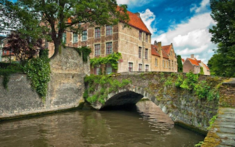 Historic stone bridge and canal in Bruges, Belgium, with medieval buildings in the background.