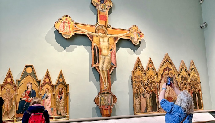Crucifix and altarpieces at Accademia Art Gallery, Florence, with visitors observing.